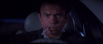 Movie still from “In the Mouth of Madness” (1994), directed by John Carpenter – A person smoking a cigarette in a car; Close Up shot, Low angle
