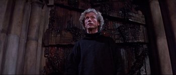Movie still from “In the Mouth of Madness” (1994), directed by John Carpenter – An older man wearing a black shirt looking up at the sky; Medium shot, Low angle