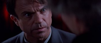 Movie still from “In the Mouth of Madness” (1994), directed by John Carpenter – A person wearing a suit and tie; Close Up shot, Over the shoulder angle