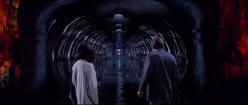 Movie still from “In the Mouth of Madness” (1994), directed by John Carpenter – A man and a woman walking through a tunnel; Wide shot, High angle