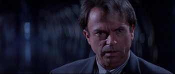 Movie still from “In the Mouth of Madness” (1994), directed by John Carpenter – A person wearing a suit and tie; Close Up shot, Low angle