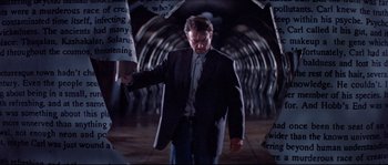 Movie still from “In the Mouth of Madness” (1994), directed by John Carpenter – A man in a suit and tie walking through a tunnel; Medium shot, Low angle