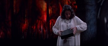 Movie still from “In the Mouth of Madness” (1994), directed by John Carpenter – A woman holding a black box in front of a fire background; Medium shot, Low angle