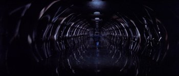 Movie still from “In the Mouth of Madness” (1994), directed by John Carpenter – A person is walking in a dark tunnel; Extreme Wide shot, High angle