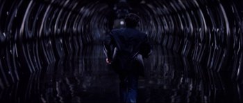 Movie still from “In the Mouth of Madness” (1994), directed by John Carpenter – A man walking in a dark tunnel of water; Wide shot, High angle