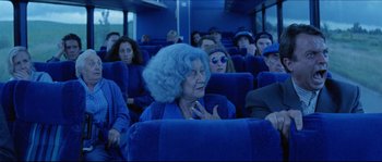Movie still from “In the Mouth of Madness” (1994), directed by John Carpenter – An older woman with blue hair sitting on a blue bus; Wide shot, High angle