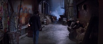 Movie still from “In the Mouth of Madness” (1994), directed by John Carpenter – A man walking down a street in an industrial setting; Wide shot, High angle