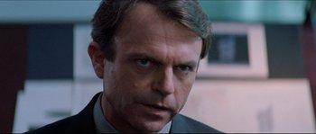 Movie still from “In the Mouth of Madness” (1994), directed by John Carpenter – A person wearing a suit and tie; Close Up shot, Over the shoulder angle