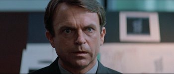 Movie still from “In the Mouth of Madness” (1994), directed by John Carpenter – A person wearing a suit and tie; Close Up shot, Over the shoulder angle