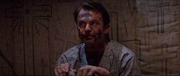 Movie still from “In the Mouth of Madness” (1994), directed by John Carpenter – A man with crosses drawn on his face; Close Up shot, High angle