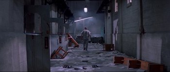 Movie still from “In the Mouth of Madness” (1994), directed by John Carpenter – A man walking through a room filled with debris; Extreme Wide shot, High angle