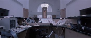 Movie still from “In the Mouth of Madness” (1994), directed by John Carpenter – A clock tower in the middle of a cluttered room; Wide shot, Low angle