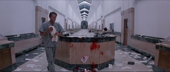 Movie still from “In the Mouth of Madness” (1994), directed by John Carpenter – A man standing next to a counter in a room; Wide shot, Low angle