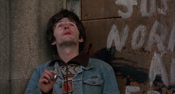 Movie still from “In the Name of the Father” (1993), directed by Jim Sheridan – A man in a jean jacket smoking a cigarette in front of a wall; Close Up shot, Overhead angle