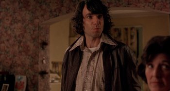 Movie still from “In the Name of the Father” (1993), directed by Jim Sheridan – A man with long black hair wearing a brown jacket; Medium shot, Over the shoulder angle