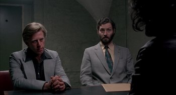 Movie still from “In the Name of the Father” (1993), directed by Jim Sheridan – Two men sitting at a table in front of another man; Medium shot, Over the shoulder angle