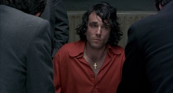 Movie still from “In the Name of the Father” (1993), directed by Jim Sheridan – A man in a red shirt with a cross on his neck; Close Up shot, Over the shoulder angle
