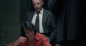 Movie still from “In the Name of the Father” (1993), directed by Jim Sheridan – A man in a suit standing next to another man in an orange shirt; Medium shot, Over the shoulder angle