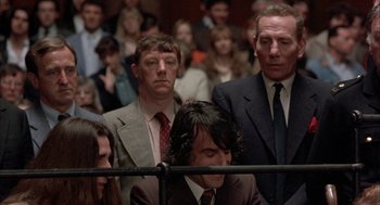 Movie still from “In the Name of the Father” (1993), directed by Jim Sheridan – A group of people in suits and ties in a room; Medium shot, Over the shoulder angle