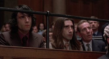 Movie still from “In the Name of the Father” (1993), directed by Jim Sheridan – A man with long hair sitting next to another man in a courtroom; Medium shot, Low angle