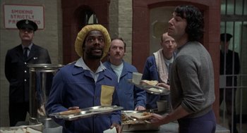 Movie still from “In the Name of the Father” (1993), directed by Jim Sheridan – A group of men standing around a table with trays of food on it; Medium shot, Over the shoulder angle