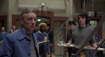 Movie still from “In the Name of the Father” (1993), directed by Jim Sheridan – A group of men standing next to each other holding plates; Medium shot, Over the shoulder angle