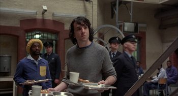 Movie still from “In the Name of the Father” (1993), directed by Jim Sheridan – A man holding a tray of food in front of a group of people; Medium shot, Over the shoulder angle