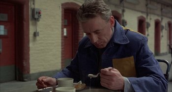 Movie still from “In the Name of the Father” (1993), directed by Jim Sheridan – A man sitting at a table with a spoon in his hand; Close Up shot, High angle