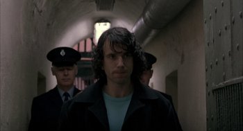 Movie still from “In the Name of the Father” (1993), directed by Jim Sheridan – A man with long curly hair wearing a black jacket; Close Up shot, Over the shoulder angle