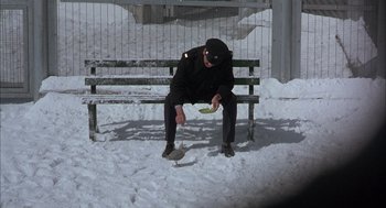 Movie still from “In the Name of the Father” (1993), directed by Jim Sheridan – A man sitting on top of a bench eating a banana; Wide shot, High angle