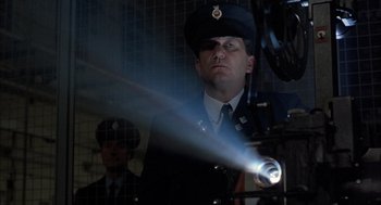Movie still from “In the Name of the Father” (1993), directed by Jim Sheridan – A man in a military uniform is looking at a flashlight; Medium shot, Low angle