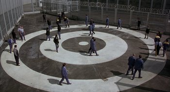 Movie still from “In the Name of the Father” (1993), directed by Jim Sheridan – A group of people walking across a circle in the middle of a courtyard; Extreme Wide shot, High angle