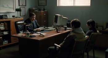 Movie still from “Incendies” (2010), directed by Denis Villeneuve – Two people sitting at a desk in a room; Wide shot, Over the shoulder angle