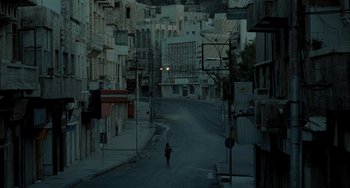 Movie still from “Incendies” (2010), directed by Denis Villeneuve – A person walking down a street near a building; Extreme Wide shot, High angle