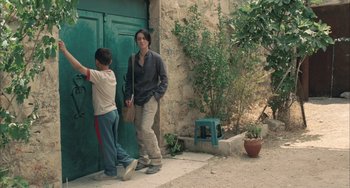 Movie still from “Incendies” (2010), directed by Denis Villeneuve – A man and a boy standing in front of a green door; Medium shot, Over the shoulder angle