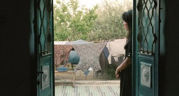 Movie still from “Incendies” (2010), directed by Denis Villeneuve – A woman standing in front of an open door with clothes hanging on a clothesline in the background; Medium shot, Over the shoulder angle