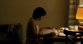 Movie still from “Incendies” (2010), directed by Denis Villeneuve – A woman sitting at a table with a book in her hands; Medium shot, High angle
