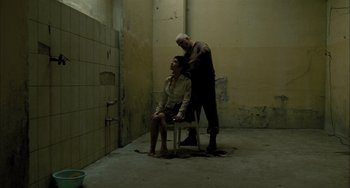 Movie still from “Incendies” (2010), directed by Denis Villeneuve – A man and a woman sitting on a chair in an empty room; Wide shot, High angle