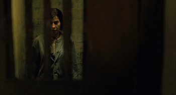 Movie still from “Incendies” (2010), directed by Denis Villeneuve – A woman standing in a dark room behind bars; Medium shot, High angle
