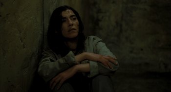 Movie still from “Incendies” (2010), directed by Denis Villeneuve – A woman sitting on the ground with her arms crossed; Close Up shot, High angle