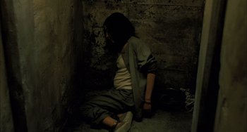 Movie still from “Incendies” (2010), directed by Denis Villeneuve – A person sitting on the ground in a room; Wide shot, High angle