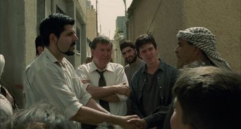 Movie still from “Incendies” (2010), directed by Denis Villeneuve – A group of men standing next to each other on a street; Medium shot, Over the shoulder angle