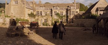 Movie still from “Far from the Madding Crowd” (2015), directed by Thomas Vinterberg – Two people are walking in front of an old building; Extreme Wide shot, High angle