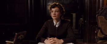 Movie still from “Far from the Madding Crowd” (2015), directed by Thomas Vinterberg – A woman sitting at a table with her hands crossed; Medium shot, Over the shoulder angle