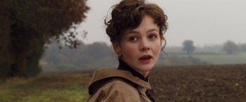 Movie still from “Far from the Madding Crowd” (2015), directed by Thomas Vinterberg – A young woman in a brown jacket is standing in a field; Close Up shot, Over the shoulder angle