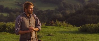 Movie still from “Far from the Madding Crowd” (2015), directed by Thomas Vinterberg – A man standing on a lush green hillside; Medium shot, Over the shoulder angle