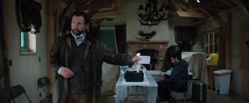 Movie still from “In the Earth” (2021), directed by Ben Wheatley – A man holding a piece of paper while standing next to a table; Medium shot, Low angle