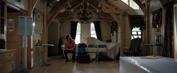 Movie still from “In the Earth” (2021), directed by Ben Wheatley – A man sitting on a chair in front of a bunch of suitcases; Wide shot, Low angle