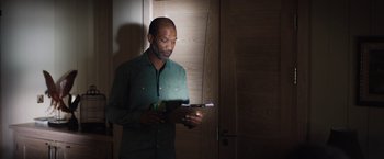 Movie still from “In the Earth” (2021), directed by Ben Wheatley – A man standing in front of a door looking at papers; Medium shot, Low angle