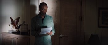 Movie still from “In the Earth” (2021), directed by Ben Wheatley – A man standing in front of a door looking at papers; Medium shot, High angle